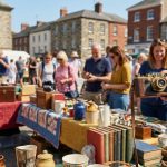 Une personne tient un appareil photo ancien sur un marché aux puces en plein air avec des stands de brocante en arrière-plan.