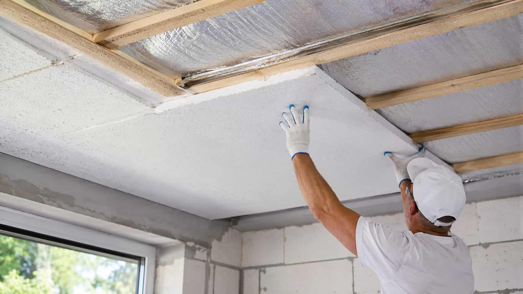 Un artisan pose une plaque isolante au plafond.